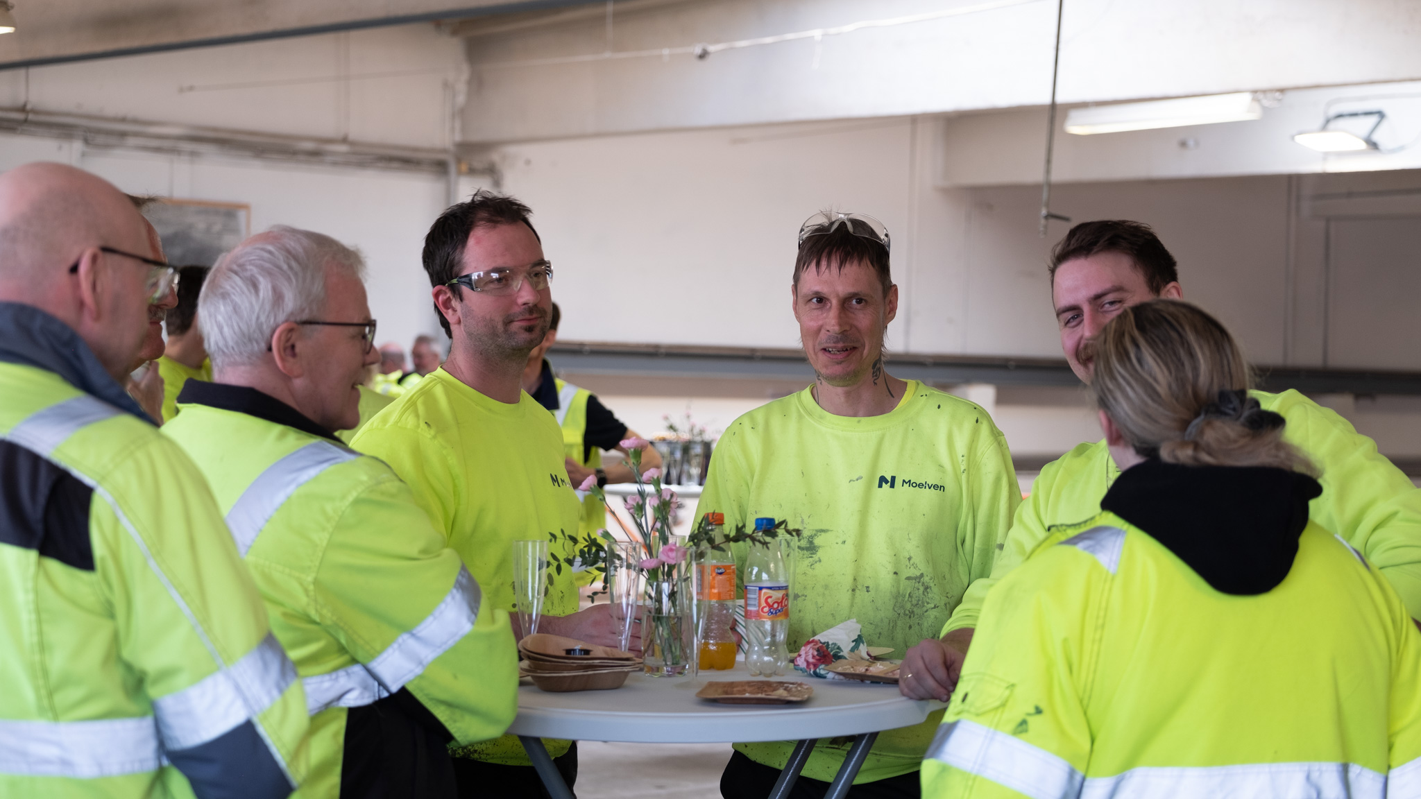 Ansatte i Moelven Langmoen rundt ståbord med festmat under 100-årsmarkering av bedriften. Foto.